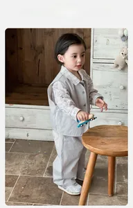 Three-piece boys outfit with grey utility vest, plaid shirt, and trousers in home setting