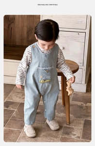Detail of baby denim overalls with cute crocodile embroidery and striped long sleeve shirt