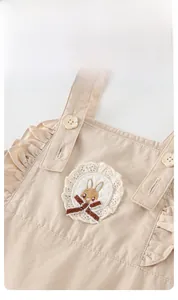 Dettaglio del vestito beige per neonata con ricami in pizzo e applicazione a coniglio