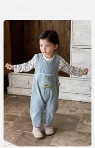 Detail of baby denim overalls with sun and crocodile embroidery and striped long sleeve shirt