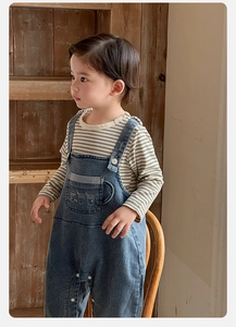 Détail de la salopette en jean pour bébé avec t-shirt rayé et boutons-pression à l'entrejambe