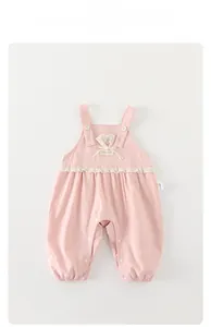Detail of pink cotton baby overalls featuring lace trim, flower buttons, and bow accents