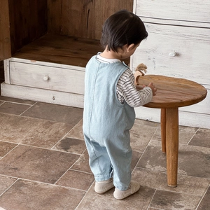 Infant denim overalls set with striped long sleeve shirt and beige shoes on a wooden stool
