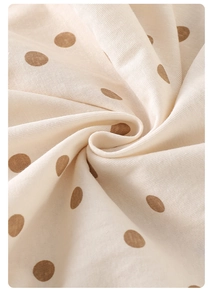 Close-up of soft cotton baby romper fabric with brown polka dots and spiral fold texture