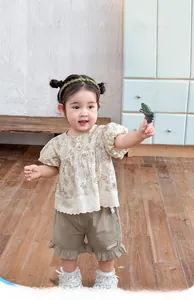 Close-up of girls beige floral top and khaki ruffle shorts set in a warm indoor setting