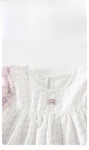 Détail de robe bébé fleurie avec manches à volants roses et broderie en coton