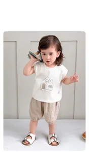 Detail of baby summer set featuring white sleeveless tee with house print and plaid shorts