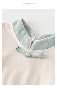 Detail of baby romper featuring a Chinese-style collar with pearl button and green trim