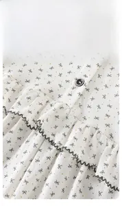 Détail d'un barboteuse bébé à fleurs avec bords à volants, pois jaunes et boutons gris