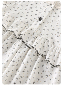 Détail de la barboteuse pour bébé avec bordure en dentelle blanche et motifs nœuds