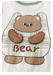 Detail of baby onesie with 3D bear appliqué and green piped neckline on soft white cotton