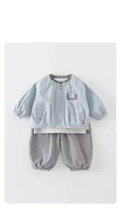 Détail d'un ensemble veste zippée bleu clair et pantalon gris pour enfant avec sourire brodé
