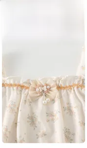 Détail d'un body fleuri pour bébé avec col à volants, nœud et pendentif perle