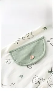 Detail of baby cotton romper featuring dinosaur prints and green pocket with wooden button
