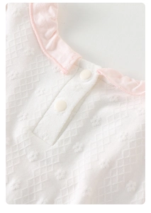 Détail du col volanté rose et du tissu jacquard blanc sur le body pour bébé fille