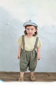 Detail eines Baby-Sommeroutfits mit gelbem T-Shirt und karierter Latzhose kurz