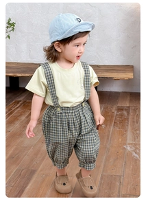 Detail von Baby-Outfit mit grünem T-Shirt, karierter Latzhose und Koala-Kinderschuhen