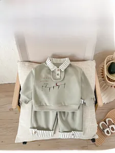 Detail of sage green kids' polo set showing striped trim and bird embroidery