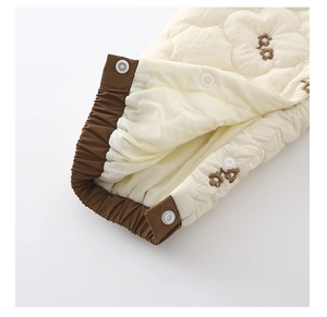 Détail de la broderie florale matelassée et des poignets élastiques sur la barboteuse bébé