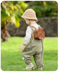 Outdoor shot of a toddler wearing olive green overalls and a brown ladybug backpack