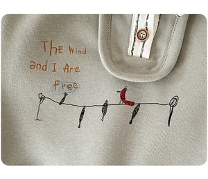Detail of light grey-green knitted toddler top with cute bird print and button collar