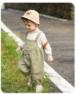 Detail of baby overalls with dog pocket and a beige sun hat with smiling face embroidery