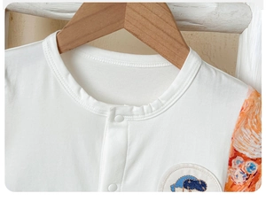 Detail of baby romper featuring round neck, white resin buttons and artistic orange sleeves