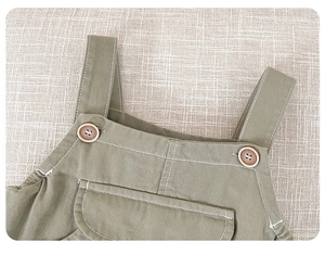 Detail of baby cotton overalls featuring vintage wooden buttons and a front pocket design