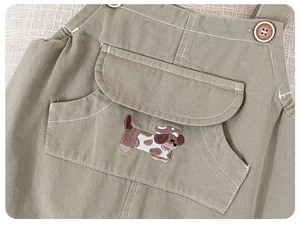 Detail of baby overalls featuring cute puppy embroidery and natural wood buttons