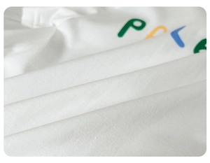 Detail of soft white cotton baby romper featuring colorful PCLE letter printing