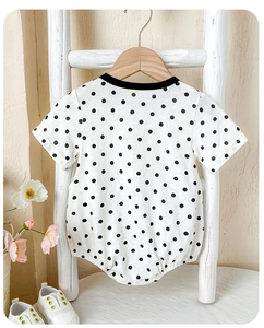 Detail of short-sleeve cotton baby bodysuit with black polka dots on wooden hanger