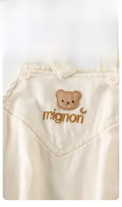 Detailaufnahme des Baby-Stramplers mit Bärenstickerei, Mignon-Schriftzug und Knöpfen