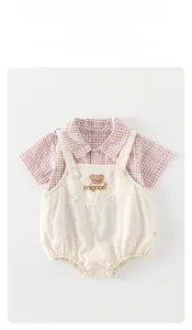 Detail eines Baby-Sommersets mit Bärenstickerei auf beiger Latzhose und Karohemd