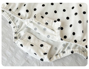 Detail of baby cotton romper with black polka dots and three snap button closures
