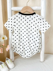 Short sleeve baby cotton romper with black polka dots on white on a wooden hanger