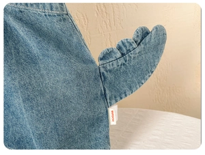 Détail d'une tenue en denim pour bébé avec motif de queue de dinosaure 3D et coutures