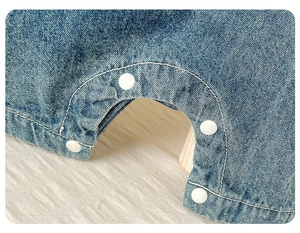 Détail de la barboteuse en denim pour bébé avec boutons-pression blancs à l'entrejambe
