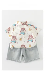 Detail of short-sleeved cream shirt with cartoon prints and light blue denim shorts for boys