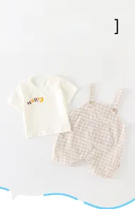 Detail of baby cotton summer set featuring white T-shirt and brown checkered overalls