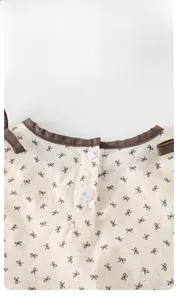 Detail of the baby floral top featuring a brown bow pattern and a white button neckline