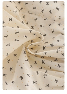 Close-up of soft cotton fabric with black bow patterns and orange polka dots for toddler set