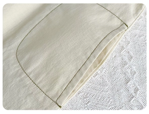 Detail of baby romper pocket with contrast olive stitching on cream cotton-linen fabric
