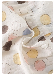Close-up of soft white cotton gauze fabric with colorful polka dots on baby bodysuit