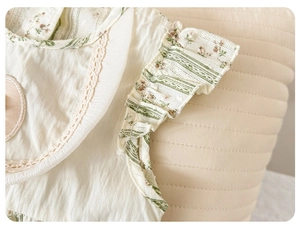 Close-up of baby romper showing cream floral fabric with lace trim and ruffled shoulders