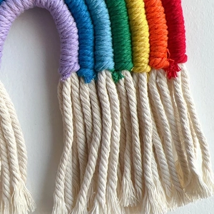 Detail of bohemian rainbow wall hanging showing colorful woven cotton ropes and soft white fringe