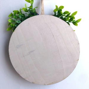 Close-up of a round wooden welcome sign base with rustic jute rope and green foliage decor