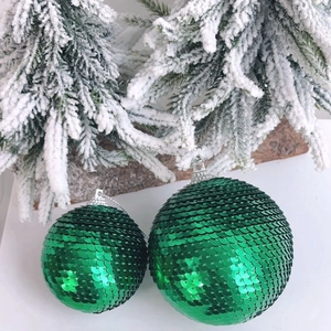 Close-up of sparkling green sequin scale Christmas ornaments on snow pine branches