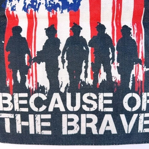 Detail of burlap garden flag with soldier silhouettes and Because of the Brave text