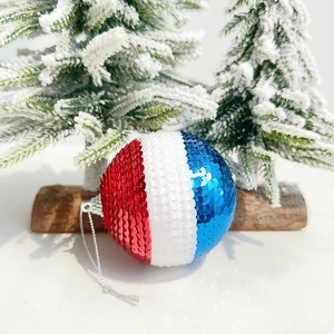 Close-up of red white and blue sequined hanging ball ornaments on snowy pine background