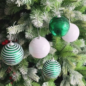 Sparkling green and white sequined Christmas ball ornaments hanging on a frosted pine tree